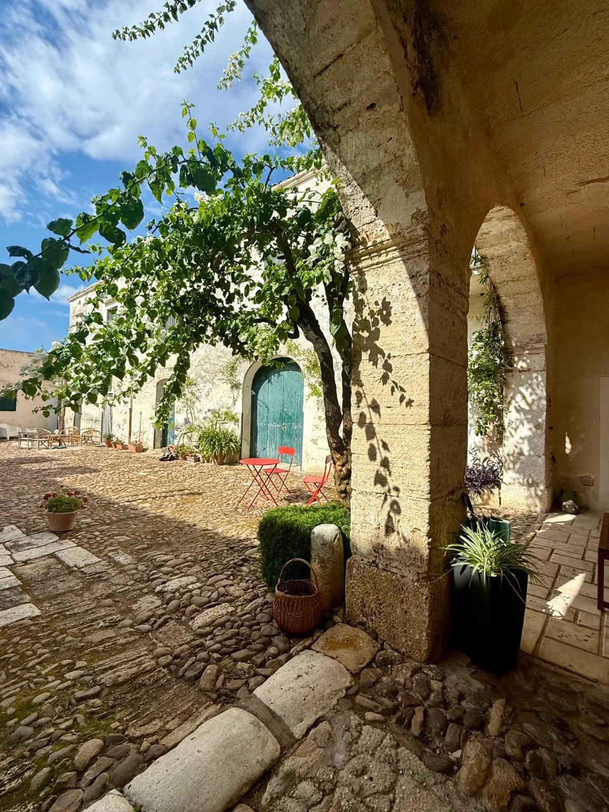 Cortile in pietra con archi, piante e una porta verde